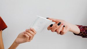 Two people exchanging a sanitary pad, symbolizing menstrual hygiene awareness.