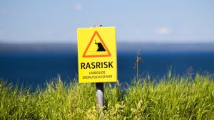 Bright warning sign for landslides in Jönköping, Sweden with scenic ocean view.